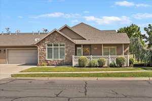 View of front of house with concrete driveway, a shingled roof, a garage, covered porch, and stone siding