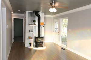 Interior space featuring wood finished floors, a wood stove, ceiling fan, and ornamental molding