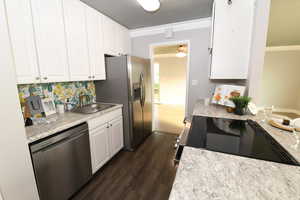 Kitchen with stainless steel dishwasher, white cabinets, dark wood-type flooring, and light countertops
