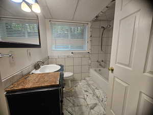 Full bath featuring marble finish flooring, vanity, tile walls, and tub / shower combination