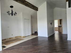 Empty room with high vaulted ceiling, a chandelier, wood finished floors, and beamed ceiling