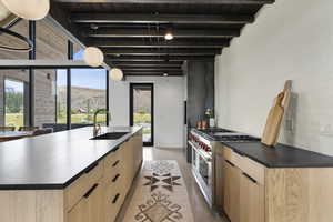 Kitchen featuring modern cabinets, light brown cabinets, a kitchen island with sink, luxury stove, and a wood ceiling with exposed beams