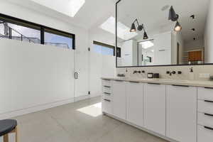 Full bath with a skylight, double vanity, a shower stall, and finished concrete floors
