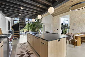 Kitchen with dark countertops, light brown cabinets, modern cabinets, a kitchen island with sink, and high end stainless steel range oven