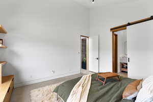 Bedroom featuring a barn door, a towering ceiling, and ensuite bath