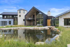 Back of house featuring a metal roof, stone siding, a chimney, a patio, and a balcony