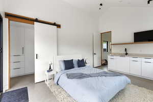 Bedroom featuring finished concrete floors, a barn door, high vaulted ceiling, and ensuite bathroom
