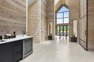 Bar area with wood walls, high vaulted ceiling, beverage cooler, concrete floors, and dark cabinets