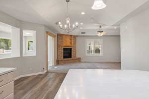 Unfurnished living room featuring lofted ceiling, plenty of natural light, a ceiling fan, wood finished floors, and a brick fireplace