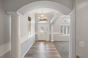 Entryway with decorative columns, a chandelier, arched walkways, crown molding, and wood finished floors