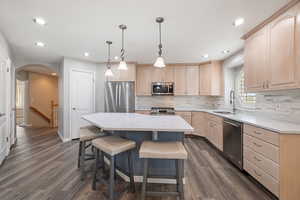 Kitchen with light brown cabinetry, arched walkways, stainless steel appliances, dark wood finished floors, and a kitchen breakfast bar