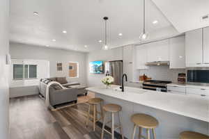 Kitchen featuring modern cabinets, dark wood-style flooring, a kitchen bar, appliances with stainless steel finishes, and recessed lighting