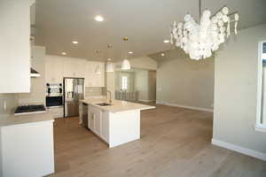 Kitchen/ Dining view featuring decorative light fixtures, appliances with stainless steel finishes, white cabinets, an island with sink, and open floor plan