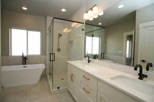 Bathroom featuring wainscoting, a soaking tub, double vanity, a stall shower, and tile walls