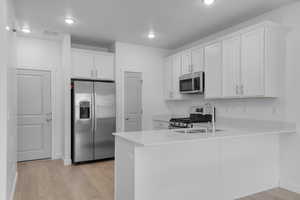 Kitchen with appliances with stainless steel finishes, a peninsula, light wood finished floors, white cabinets, and recessed lighting