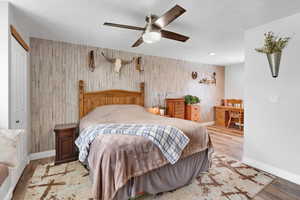 Bedroom with wood walls, light wood-style floors, and ceiling fan