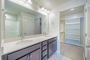 Full bath featuring double vanity, a spacious closet, and a textured ceiling