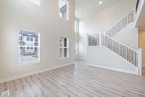 Unfurnished living room with wood finished floors, stairway, a towering ceiling, and recessed lighting