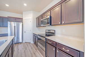 Kitchen with stainless steel appliances, light wood-style floors, light stone countertops, recessed lighting, and dark brown cabinets