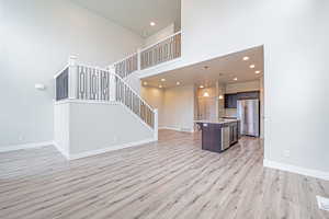 Unfurnished living room featuring a towering ceiling, light wood-type flooring, stairway, and recessed lighting
