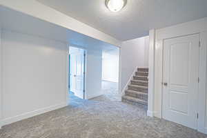 Finished below grade area with carpet floors, a textured ceiling, and stairs