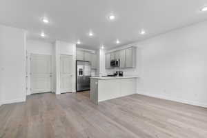 Kitchen with gray cabinets, a peninsula, stainless steel appliances, light wood-style floors, and light countertops
