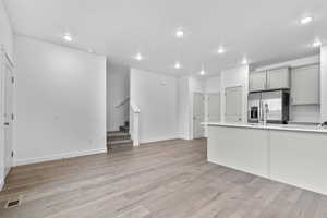 Kitchen featuring gray cabinets, stainless steel refrigerator with ice dispenser, light wood finished floors, recessed lighting, and light countertops