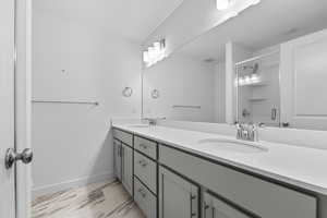 Full bathroom with double vanity, marble look tile flooring, and an enclosed shower