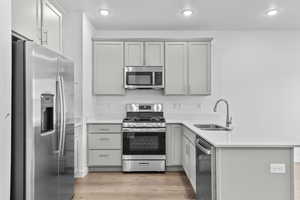 Kitchen featuring stainless steel appliances, a peninsula, gray cabinets, light wood-style floors, and light countertops