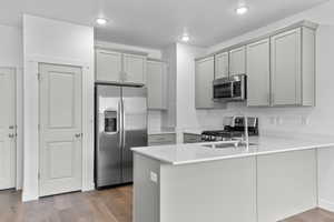 Kitchen featuring stainless steel appliances, a peninsula, gray cabinets, wood finished floors, and recessed lighting