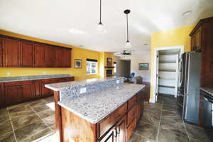 Kitchen with a center island, a ceiling fan, appliances with stainless steel finishes, decorative light fixtures, and a fireplace