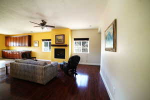 Living area with dark wood finished floors, a fireplace, and a ceiling fan