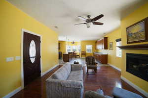Living room featuring dark wood-type flooring, ceiling fan, a textured ceiling, and a glass covered fireplace