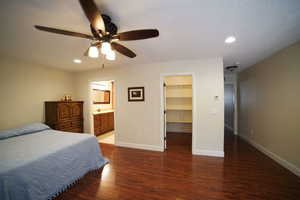 Bedroom featuring a walk in closet, wood finished floors, recessed lighting, a ceiling fan, and connected bathroom