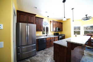 Kitchen featuring stainless steel appliances, a center island, a breakfast bar, pendant lighting, and light stone countertops