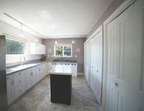 Kitchen featuring white cabinetry, a kitchen island, light countertops, freestanding refrigerator, and hanging light fixtures