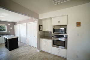 Kitchen featuring stainless steel appliances, white cabinets, light countertops, and a kitchen island