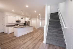 Kitchen featuring dark countertops, white cabinets, light wood-style flooring, stainless steel appliances, and a kitchen island with sink