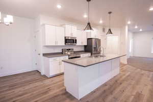 Kitchen with appliances with stainless steel finishes, an island with sink, white cabinetry, light wood finished floors, and recessed lighting