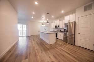 Kitchen featuring stainless steel appliances, light wood-style floors, white cabinets, recessed lighting, and an island with sink