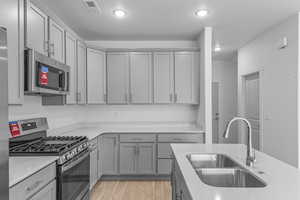 Kitchen with gray cabinetry, appliances with stainless steel finishes, light countertops, light wood-style floors, and recessed lighting