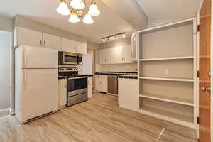Kitchen featuring backsplash, appliances with stainless steel finishes, a chandelier, white cabinets, and open shelves