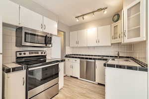 Kitchen featuring stainless steel appliances, tile countertops, backsplash, and white cabinetry
