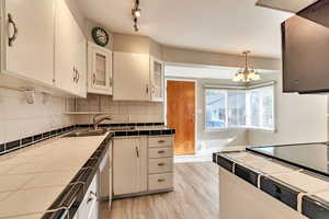 Kitchen featuring tile counters, tasteful backsplash, white cabinets, and light wood finished floors