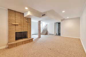 Unfurnished living room with a brick fireplace, carpet, stairway, recessed lighting, and crown molding
