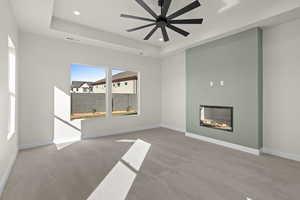 Unfurnished living room featuring carpet floors, a glass covered fireplace, ceiling fan, a raised ceiling, and recessed lighting