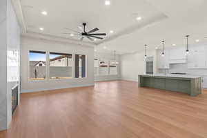 Unfurnished living room with a raised ceiling, a ceiling fan, healthy amount of natural light, and recessed lighting
