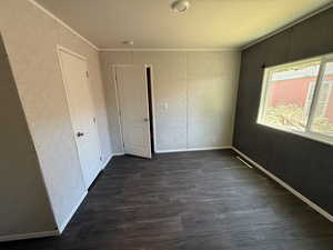 Empty room with ornamental molding, dark wood-type flooring, and a smoke detector