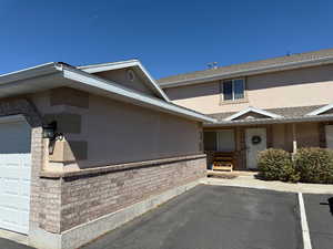 View of exterior entry with stucco siding, brick siding, and a shingled roof