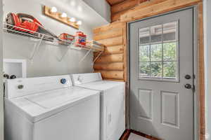 Washroom with log walls and washer and clothes dryer